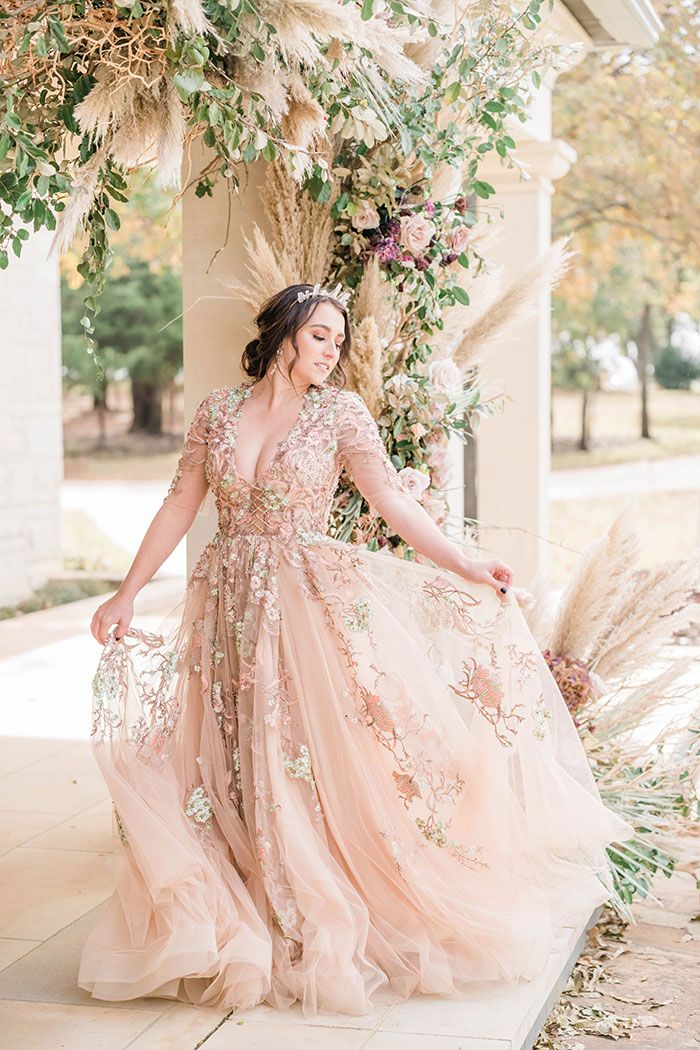 a woman in a pink dress is standing under an arch with flowers and greenery