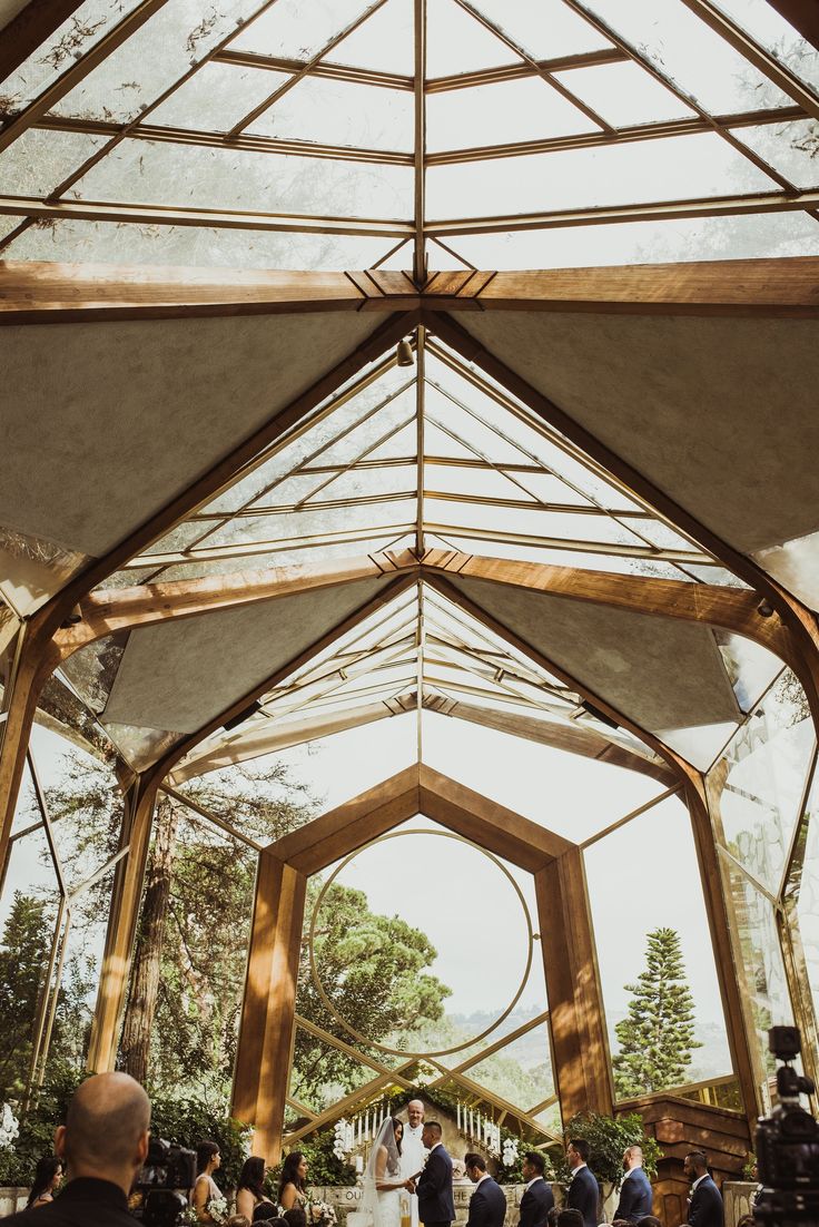 a bride and groom standing under a glass roof at their wedding ceremony in the woods