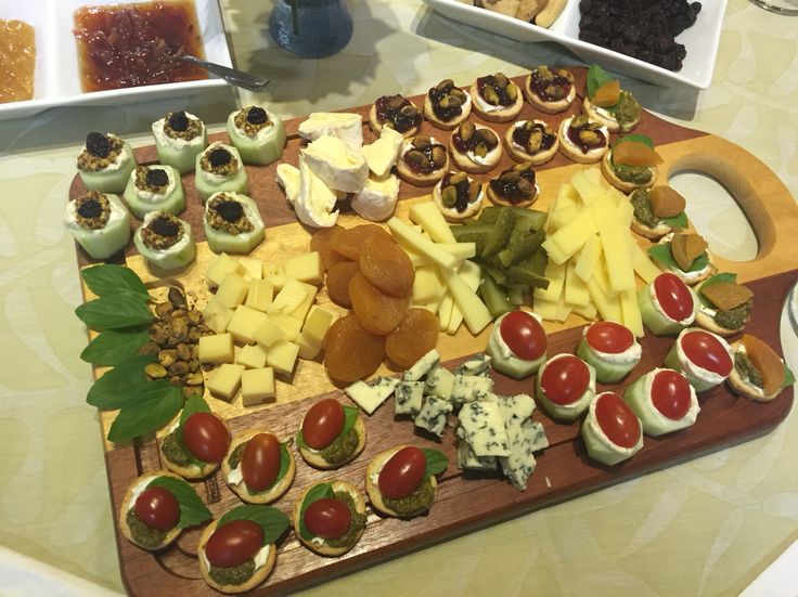 a wooden cutting board topped with lots of different types of cheeses and crackers