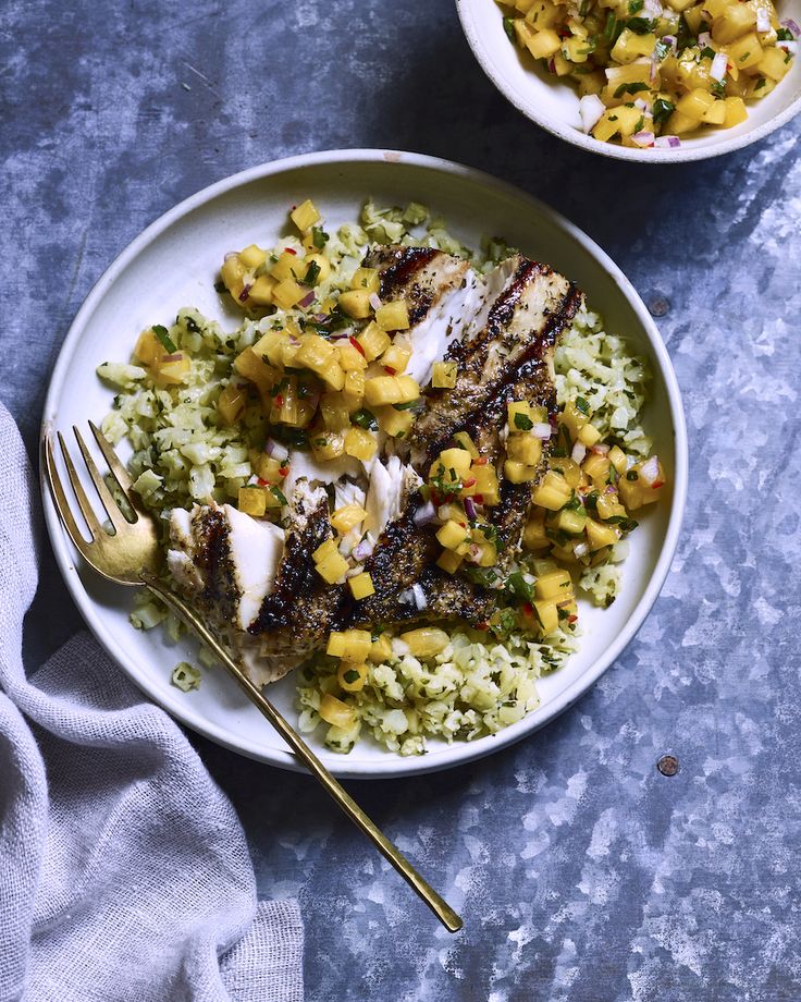 two white plates with food on them next to a silver fork and bowl filled with rice