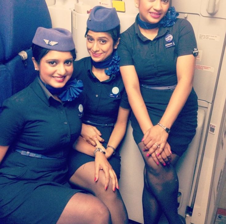 three flight attendants are sitting on an airplane's cabin door, posing for the camera