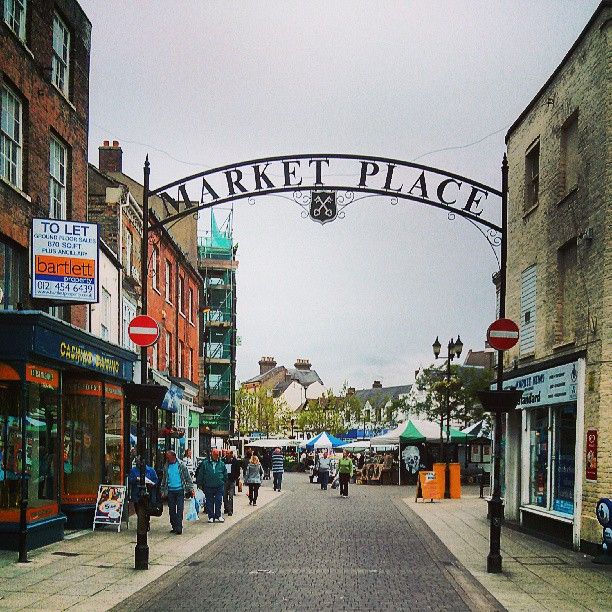 people walking down the street under an arch that says market place on it's side