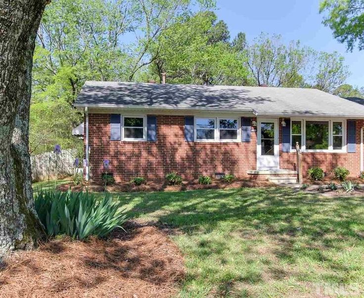 a red brick house with trees and grass in the front yard on a sunny day