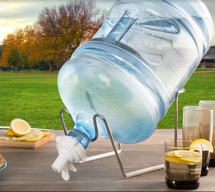 a large water bottle sitting on top of a table next to glasses and lemons