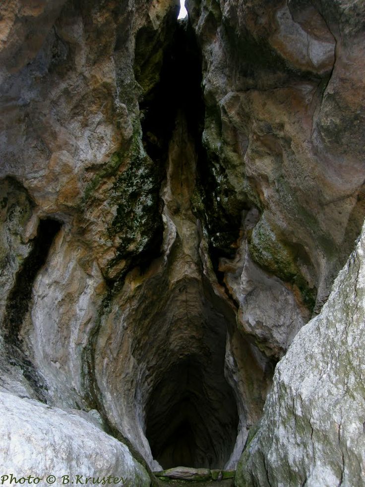 a narrow tunnel in the side of a mountain with moss growing on it's sides