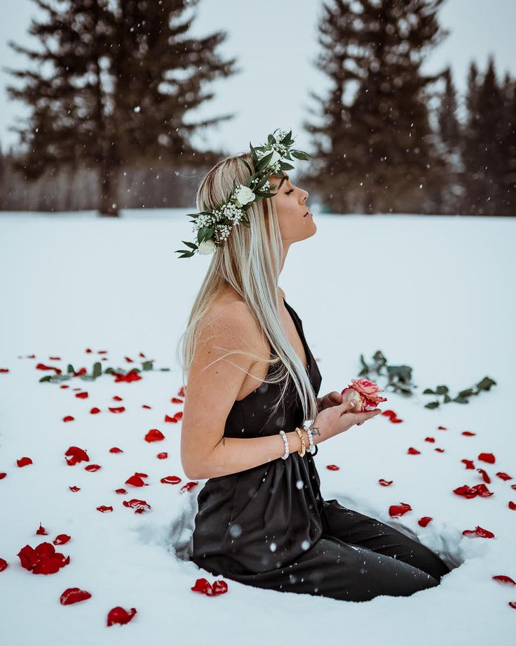 a woman sitting in the snow with flowers on her head and looking up at something