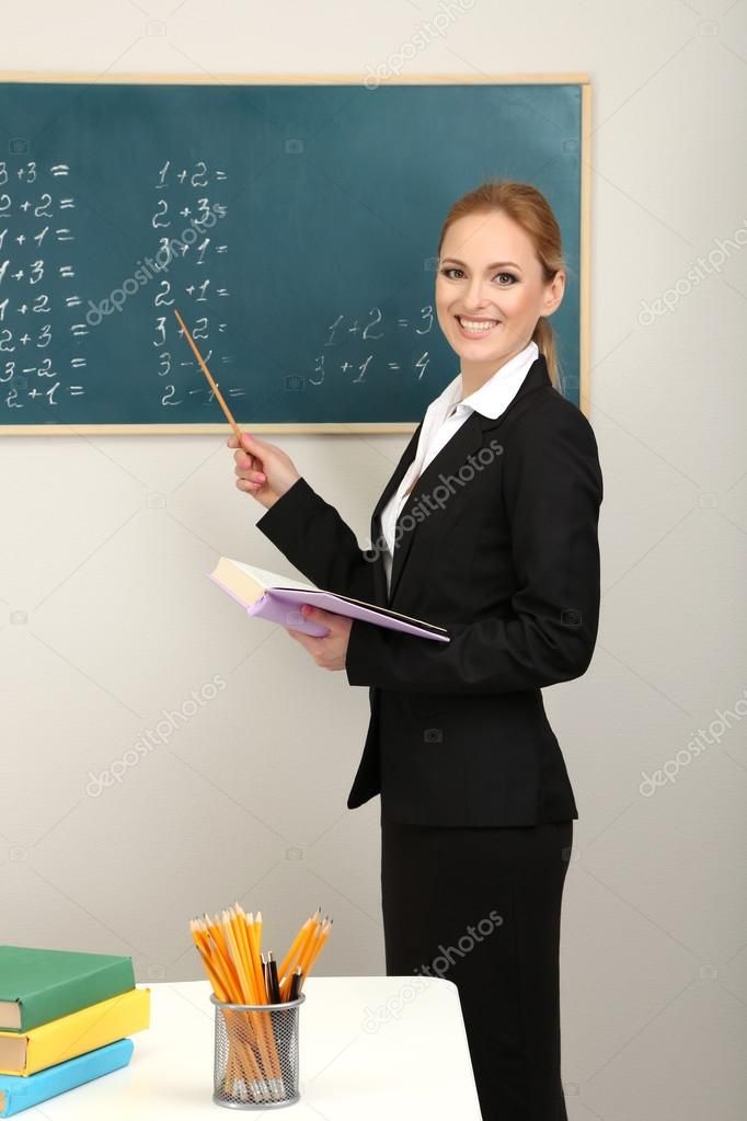 a woman teacher standing in front of a blackboard with books and pencils on it