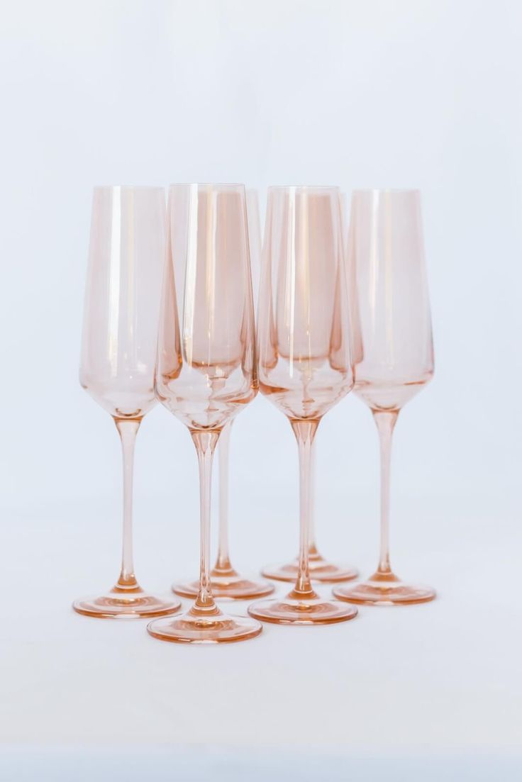 five wine glasses are lined up on a white surface, one is pink and the other has gold rims