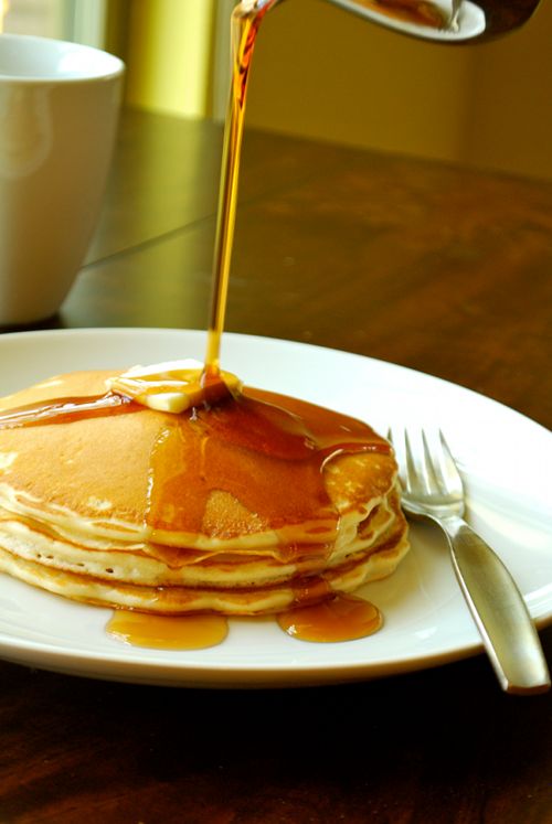 a stack of pancakes with syrup being drizzled over them on a white plate