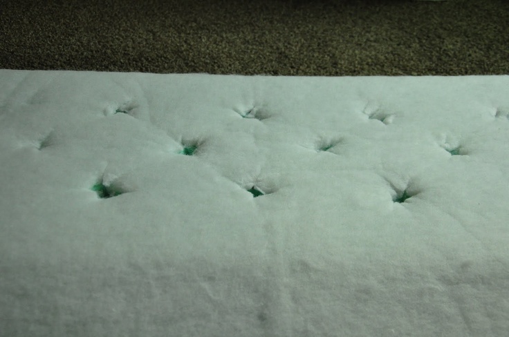 the mattress is covered with white sheets and green buttons on it's side, in front of a carpeted floor