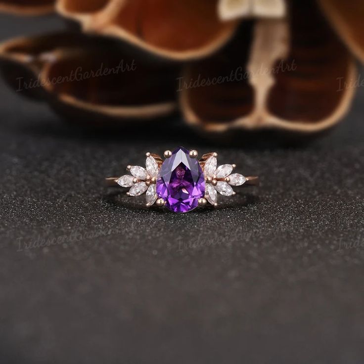 an amethoraite and diamond ring sits on a table next to some dried flowers