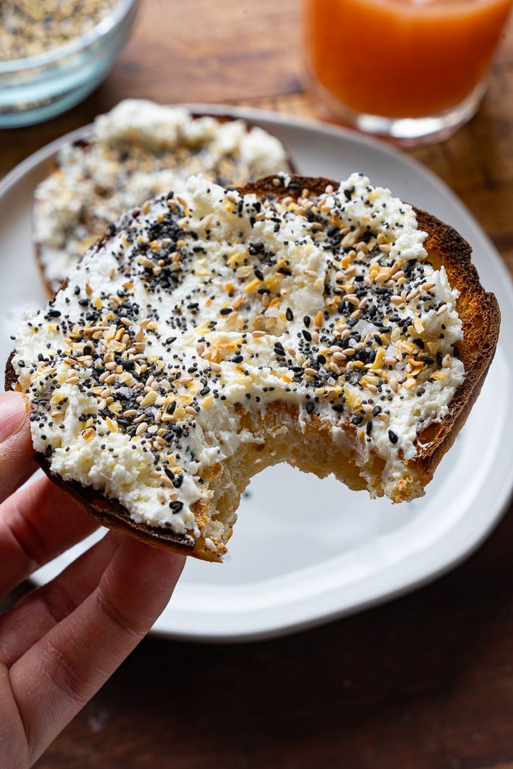 someone is holding up a piece of toast with cream cheese and black seed sprinkles