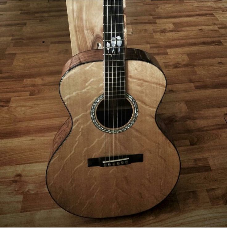 an acoustic guitar sitting on top of a hard wood floor