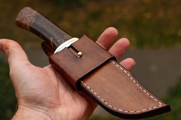 a hand holding a brown leather sheath with a knife in it's side pocket