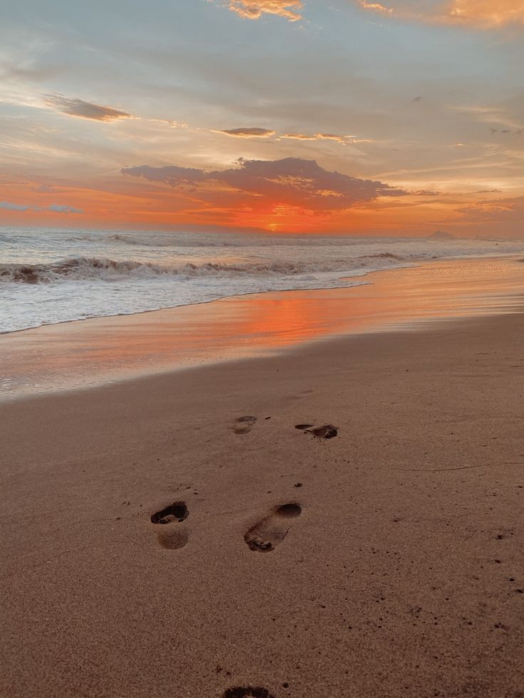 footprints in the sand on a beach at sunset