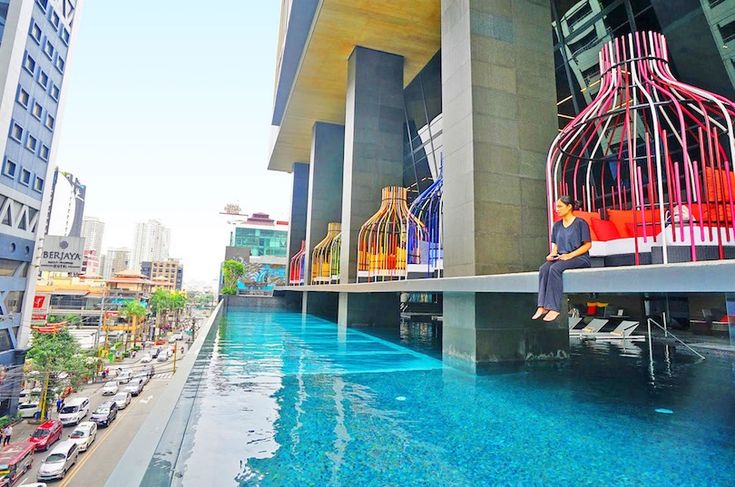 a man sitting on the edge of a swimming pool in front of a tall building