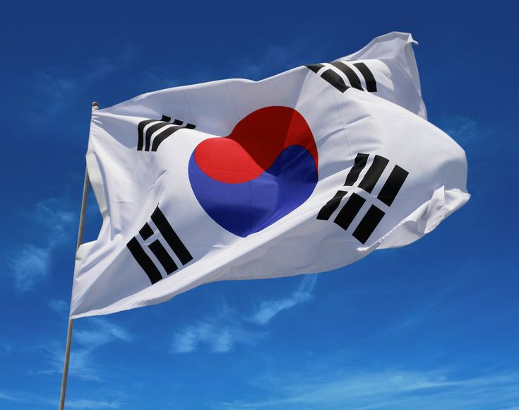 the flag of south korea flying in front of a building with people walking around it