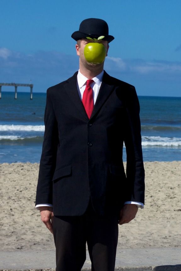 a man in a suit and tie with an apple on his face standing at the beach