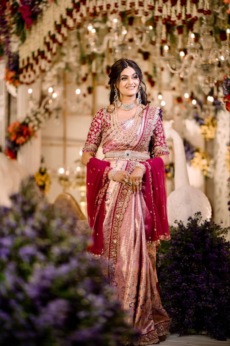 a woman in a red and gold sari standing under a chandelier filled with flowers