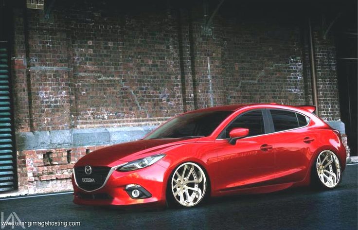 a red mazda car parked in front of a brick building with white wheels and rims