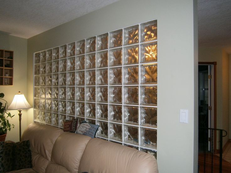 a living room filled with furniture next to a wall covered in glass block blocks and a lamp