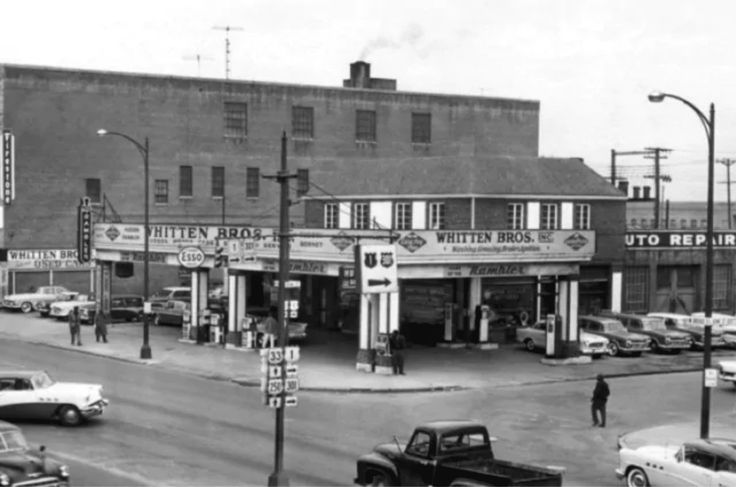 an old black and white photo of cars parked in front of a building on a street corner