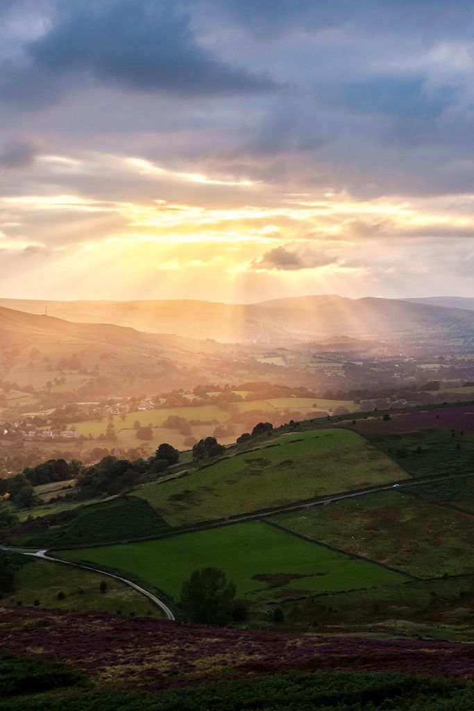 the sun shines through clouds over rolling hills and fields in rural england, with green grass on either side