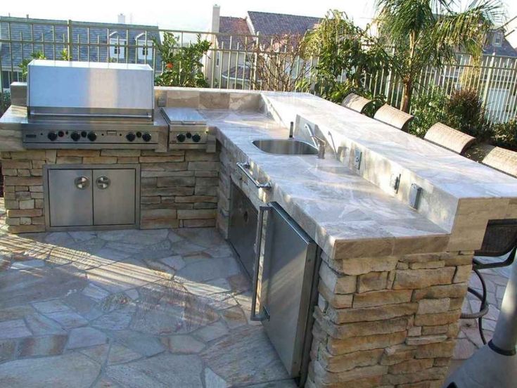 an outdoor kitchen with stone counter tops and stainless steel grilling area, surrounded by patio furniture