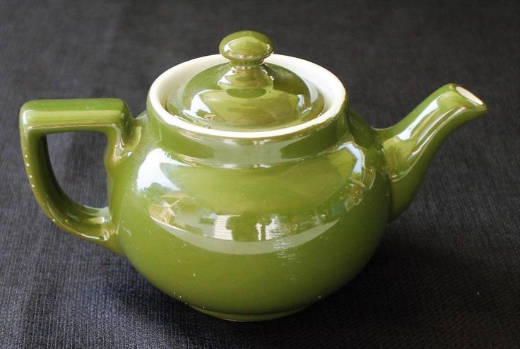 a green teapot with a white top on a black tableclothed surface in front of a dark background