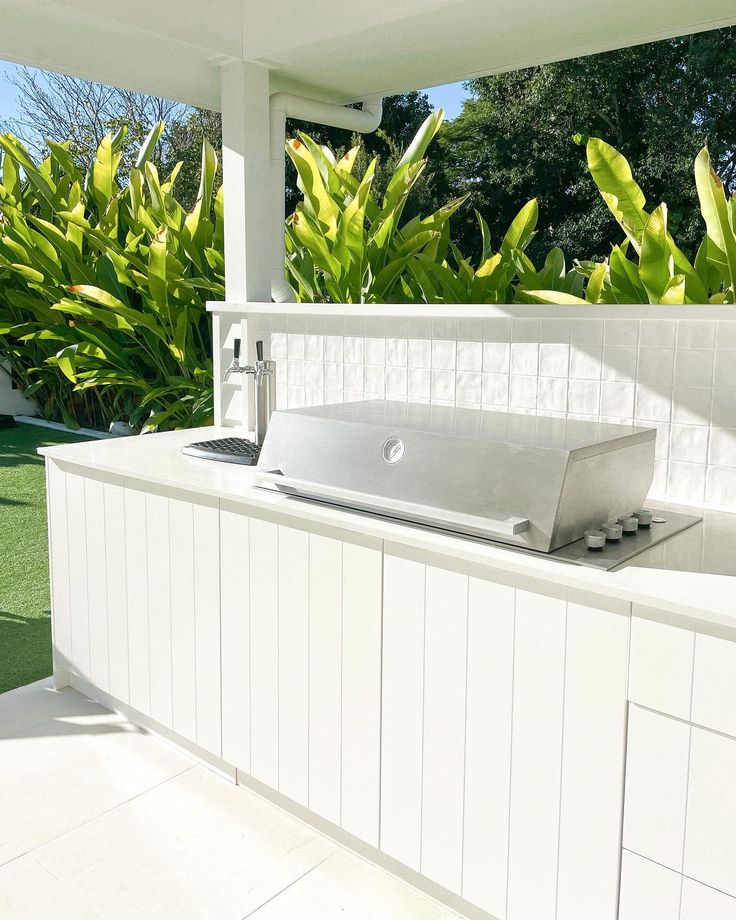 an outdoor kitchen with white cabinets and green plants in the backgroung area