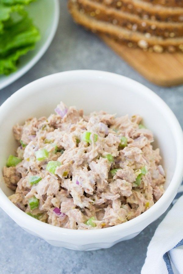 a white bowl filled with tuna salad on top of a table next to sliced bread