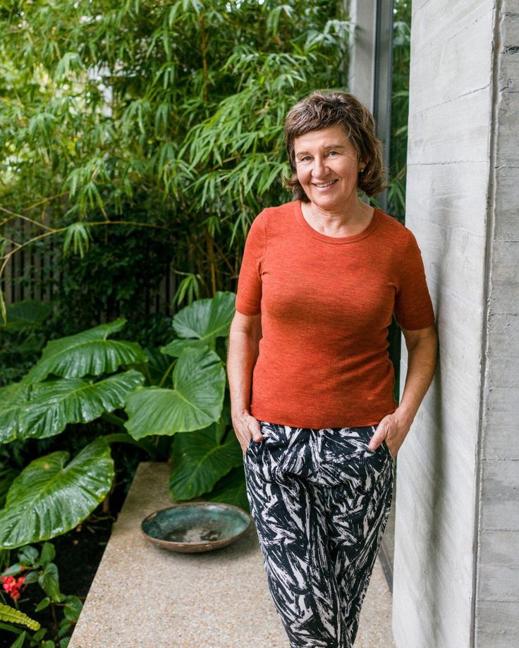 a woman leaning against the side of a building with her hands in her pockets and smiling