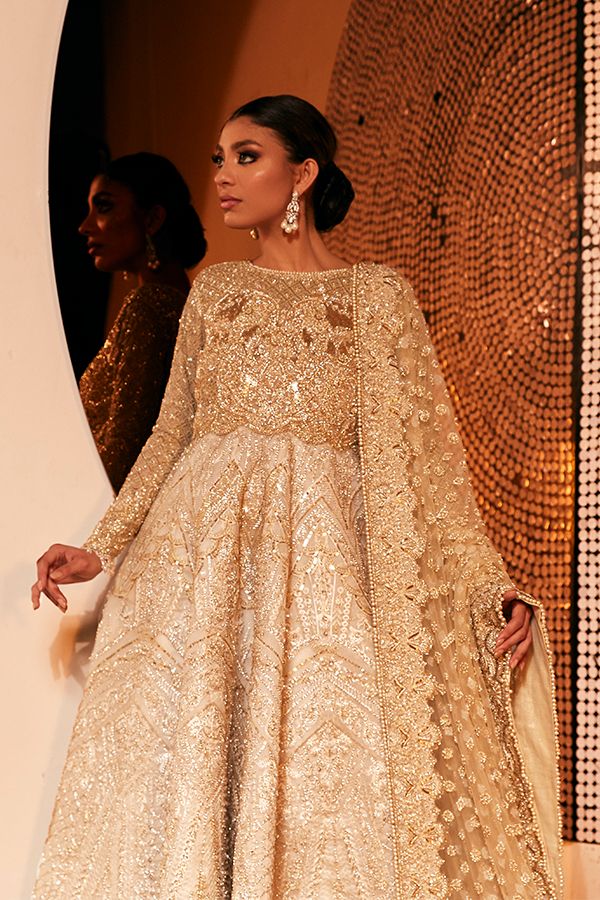 a woman in a gold gown standing next to a wall with an intricate design on it