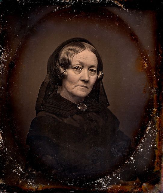 an old photo of a woman wearing a black dress with a hood over her head