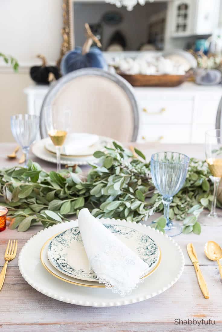 the table is set with plates, silverware and greenery