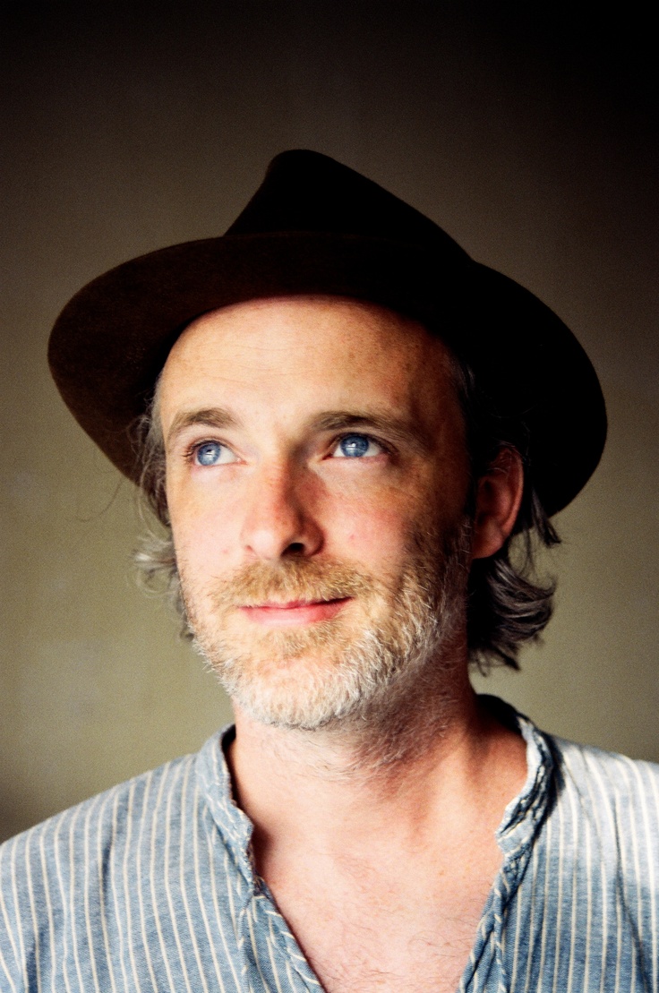 a man wearing a hat and blue eyes looks at the camera while posing for a photo