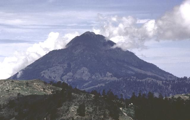 a large mountain with trees on the side and clouds in the sky over it's top