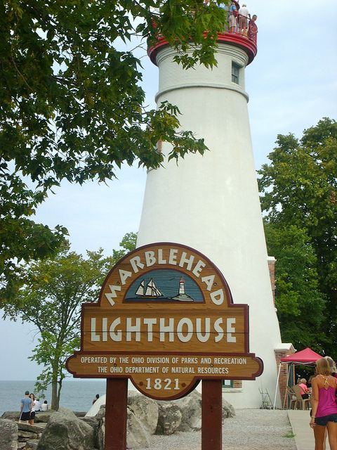 a woman standing in front of a white lighthouse with a sign that says marblehead lighthouse