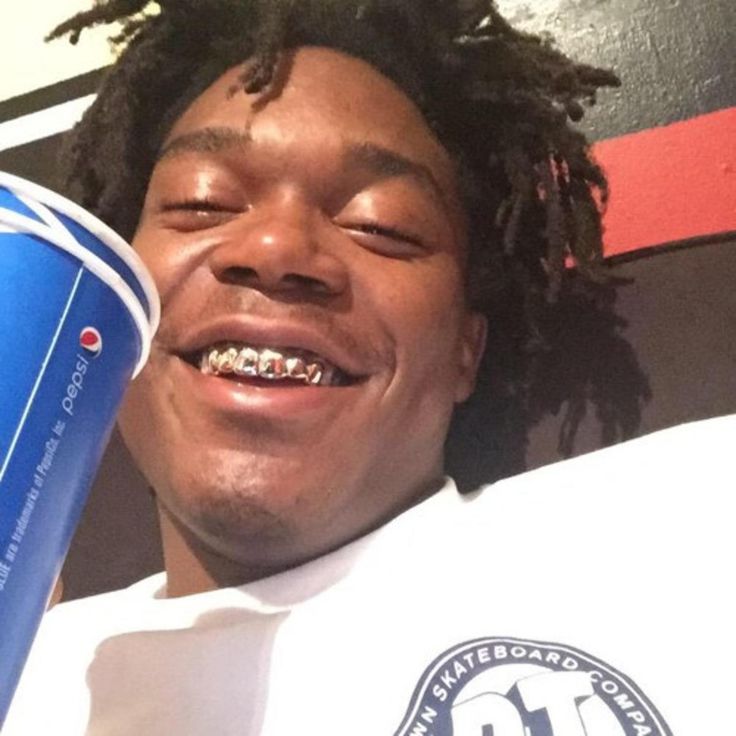 a man with dreadlocks is holding a blue cup and smiling at the camera