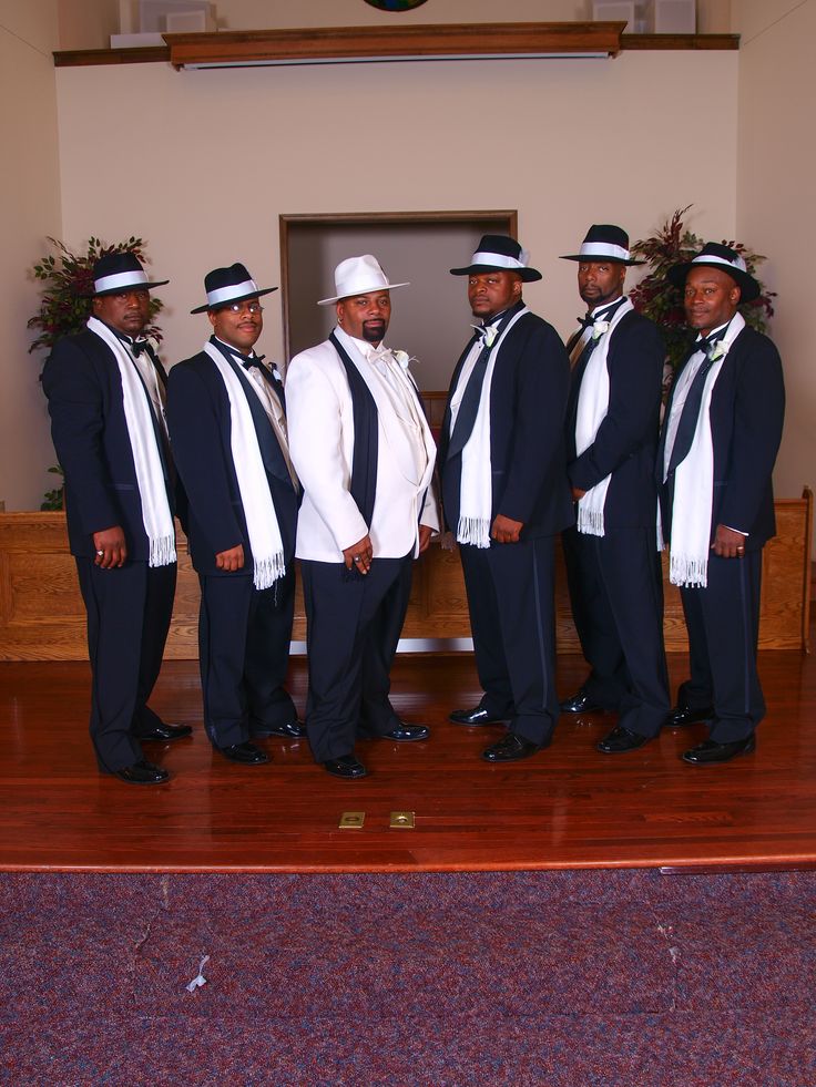 a group of men standing next to each other in front of a wooden bench wearing suits and ties