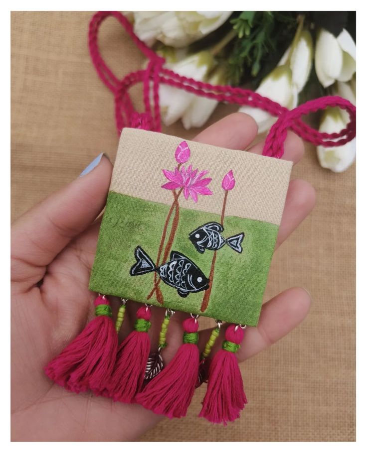 a hand holding a small piece of fabric with flowers on it and tassels