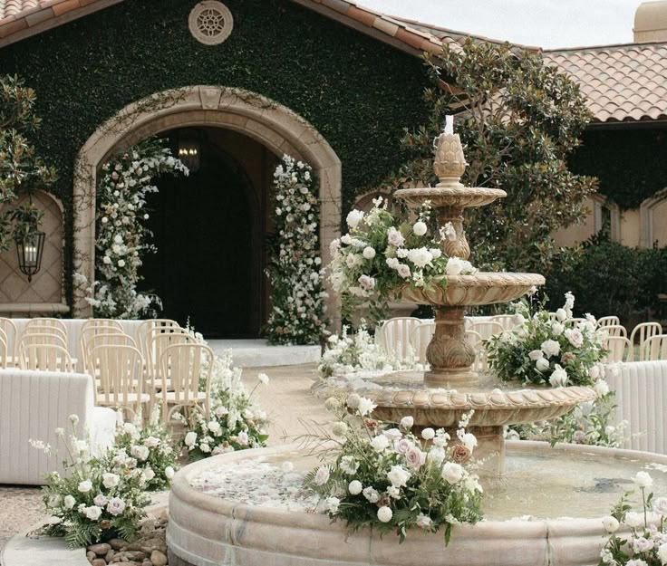 an outdoor wedding ceremony with white flowers and greenery on the side of the building