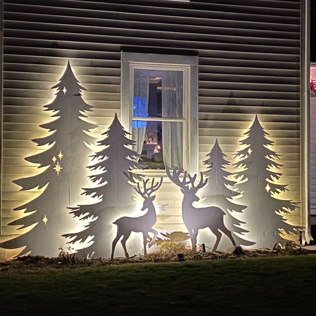 lighted christmas decorations in front of a house with deer and trees on the windowsill