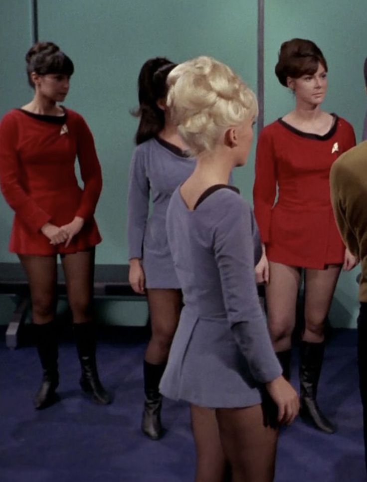 some very pretty ladies in short skirts and boots talking to each other on the set of star trek