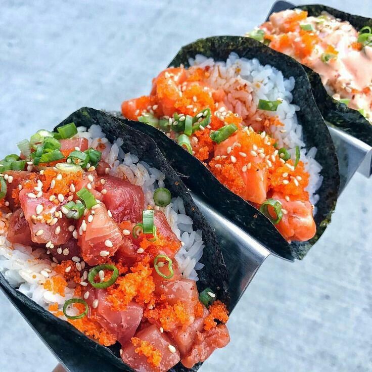 three sushi burritos with various toppings on top of rice and garnishes