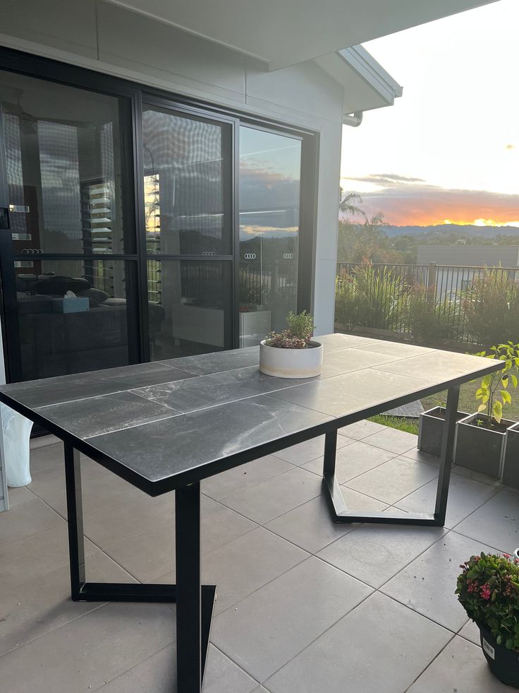 a table sitting on top of a tiled floor next to a potted plant in front of a sliding glass door