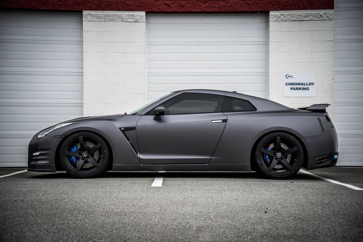 a gray sports car parked in front of a garage door with white shutters on it