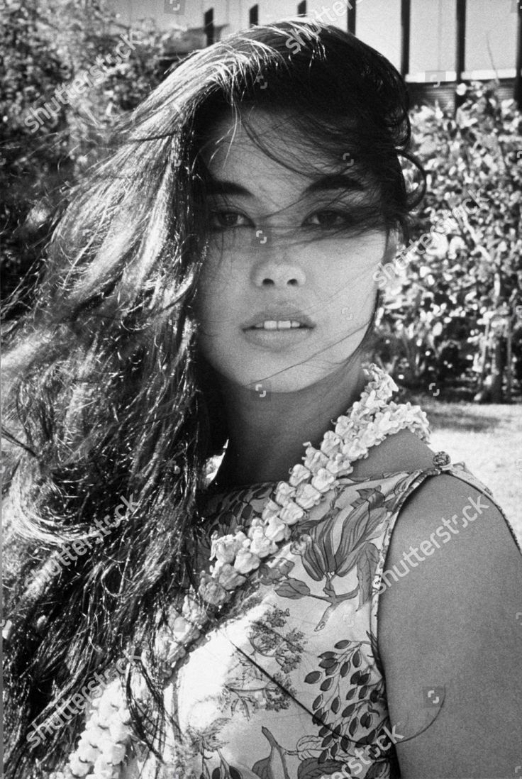 black and white photograph of a woman with long hair in front of bushes, looking at the camera