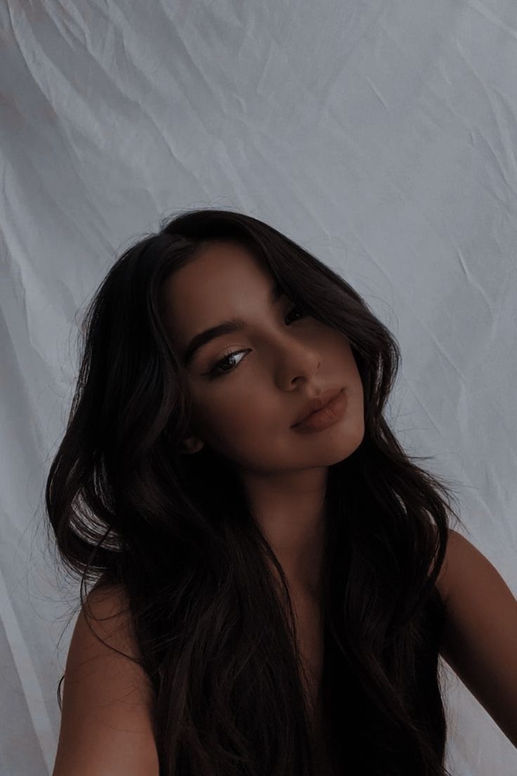 a woman with long dark hair is posing for the camera in front of a white backdrop