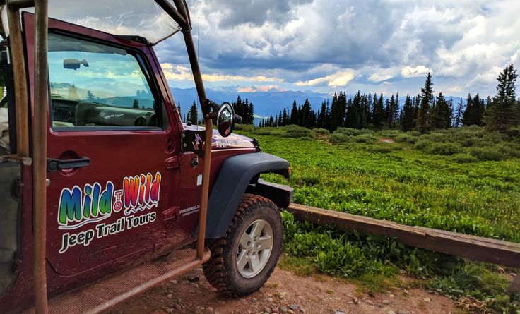 a jeep parked on the side of a dirt road with mountains in the background and clouds in the sky